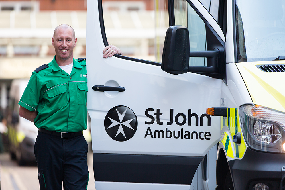 St John Ambulance male ambulance driver stands next to a open ambulance door