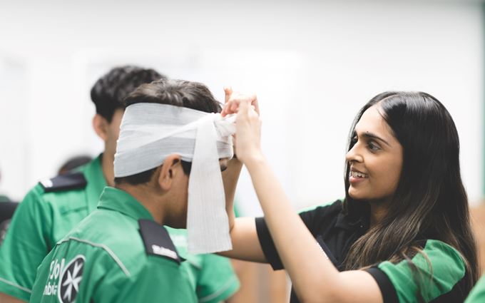 Youth Team volunteer demonstrating how to bandage a head.