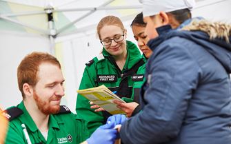 Volunteers treating patient's finger and completing paperwork in a mobile treatment centre at an event. 