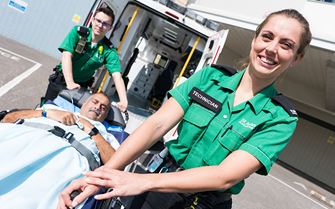 Two staff members moving a patient on a stretcher bed out of an ambulance.