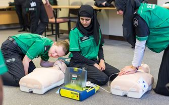 3 cadets practising doing CPR and using a defibrillator on a training manikin.