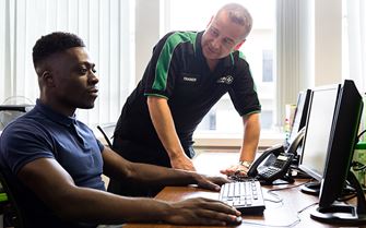 St John Ambulance trainer teaching a display screen assessment (DSE) course to a man sitting down using a computer.