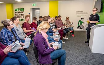  Group of people listening to a St John Ambulance trainer presenting a health and safety basics course. 