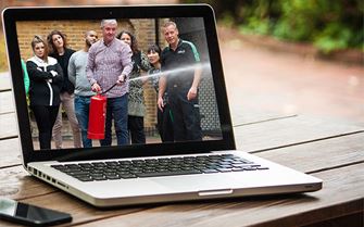 A man practicing using a fire extinguisher during a fire marshal course is displayed on a laptop screen.