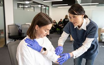 First aider applying a bandage to a casualty arm sitting down in a chair on a first aid training course. 