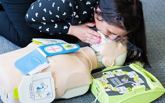 First aider performs resuscitation on a training dummy, connected to a defibrillator during a training course. 