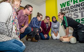 Trainer demonstrating how to give compressions on a training dummy to students in a first aid training course. 