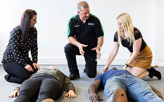 Trainer teaching how to check if a casualty is conscious during a first aid training course.