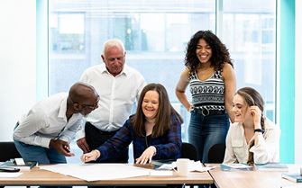 Class participants smiling around a table on a mental health training course. 