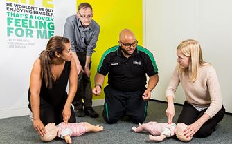 Trainer explaining infant CPR using a baby training mannequin to class members on a Paediatric first aid course.