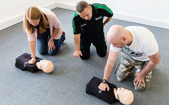  St John Ambulance trainer teaches two participants child CPR on a child training mannequin.